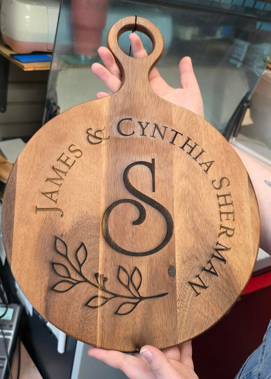 Wooden cutting board with engraved names and design held by a person.